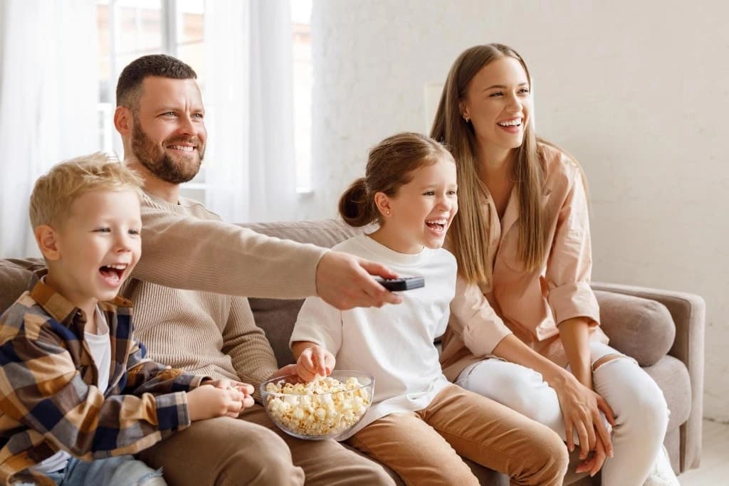 A family laughing on the sofa while the dad changes the channel with the remote