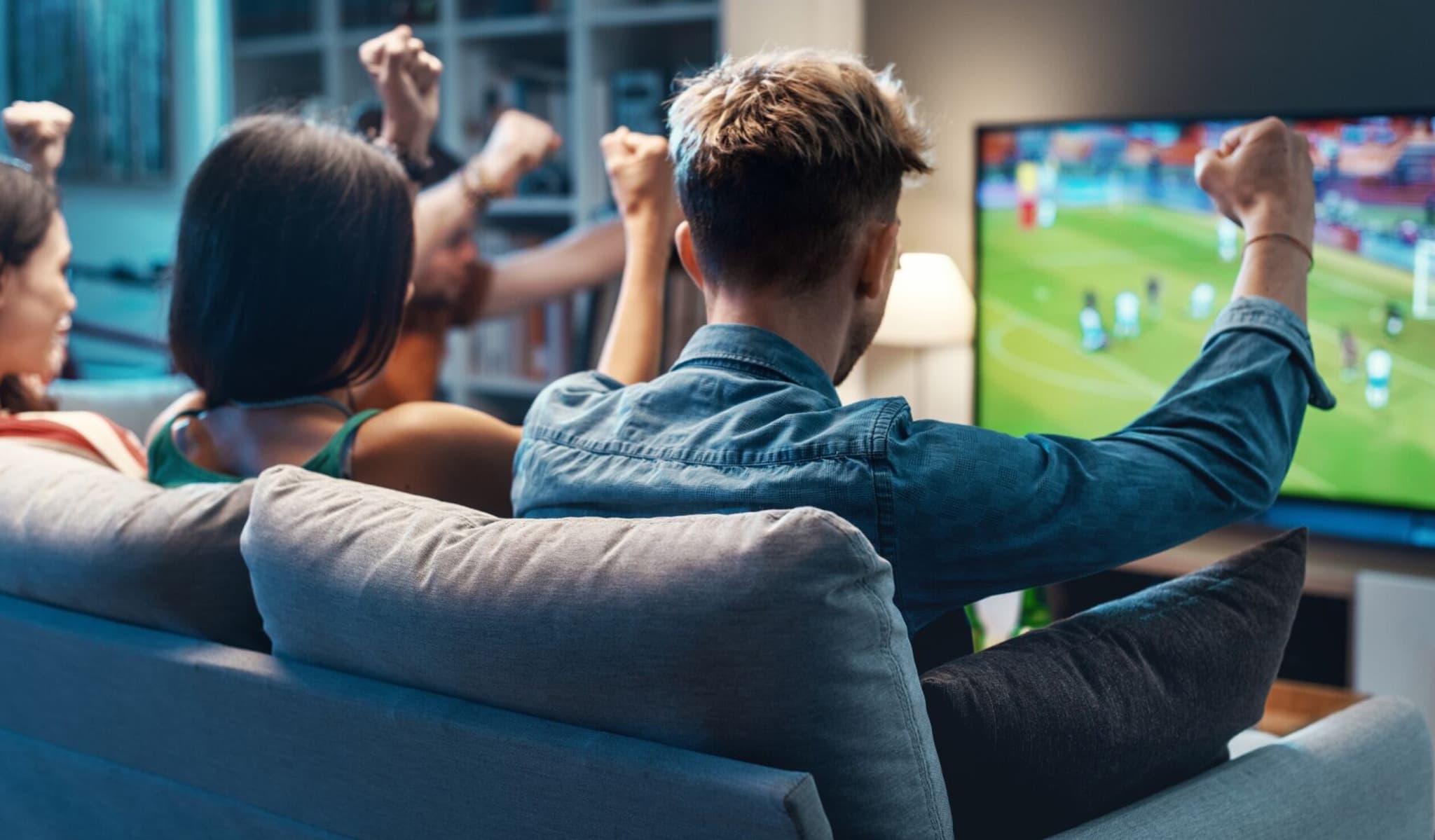 Friends on a sofa cheering a live game on their TV